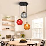 Hanglamp met drie rode, oranje en grijze glazen bollen boven een eettafel